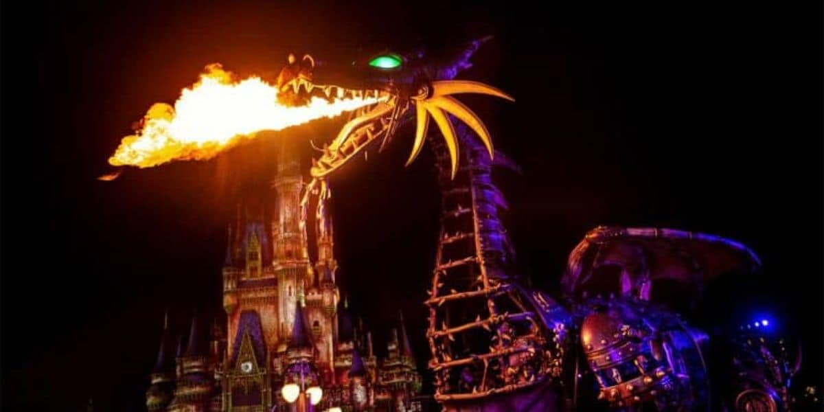 A large, illuminated dragon float breathes fire during a nighttime parade at Disney's Hollywood Studios, with a castle visible in the background, all set against a dark sky. It feels like a scene from Club Villain, where Disney Villains come to life in spectacular fashion.