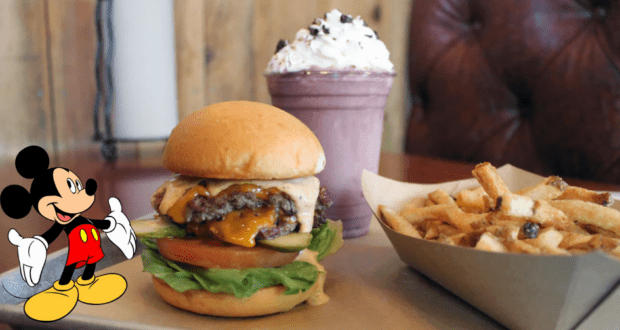 Mickey Mouse stands beside a classic burger, fries, and milkshake on a restaurant table, capturing the whimsical dining magic guests love at Disney World.