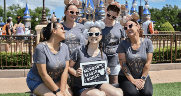 Morgan's Magic Squad brings infectious energy to Disney World, as five friends in coordinated shirts and classic mouse ears beam with excitement, proudly displaying their group sign and capturing the magic of a wedding celebration at the park.