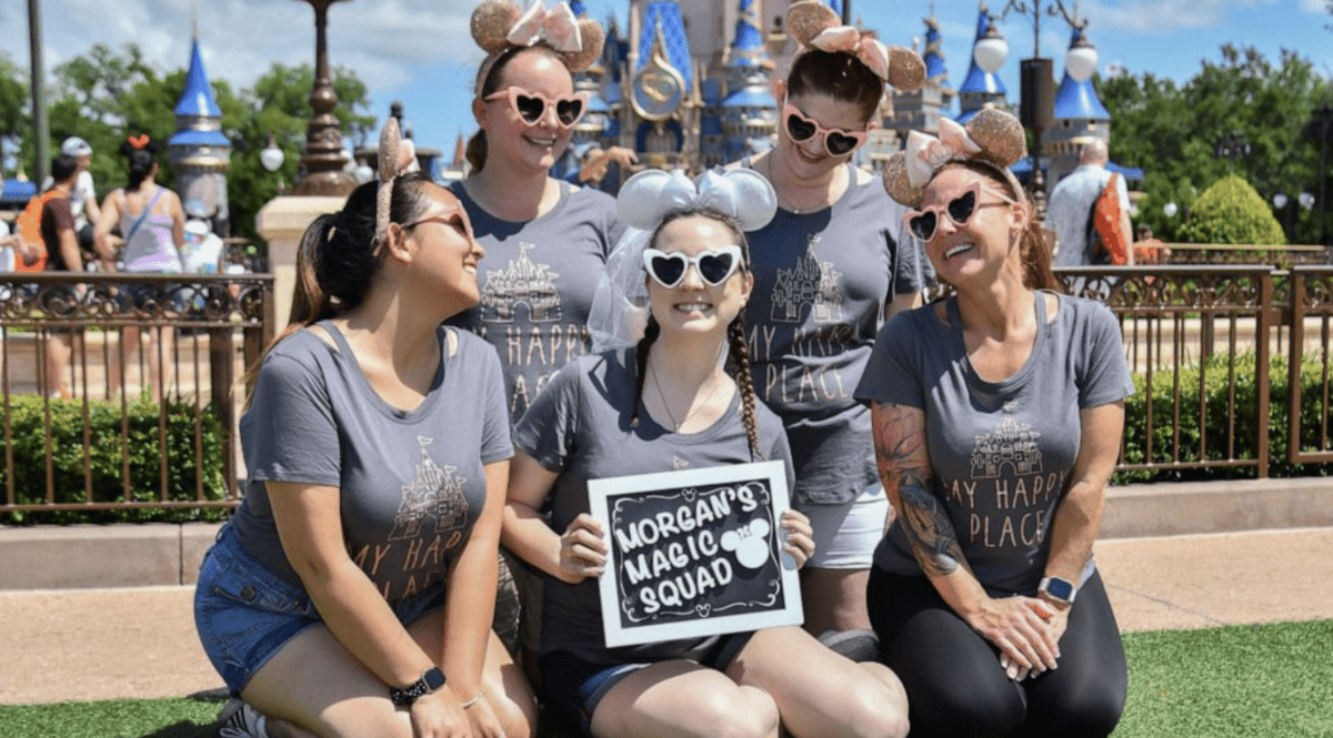 Morgan's Magic Squad brings infectious energy to Disney World, as five friends in coordinated shirts and classic mouse ears beam with excitement, proudly displaying their group sign and capturing the magic of a wedding celebration at the park.