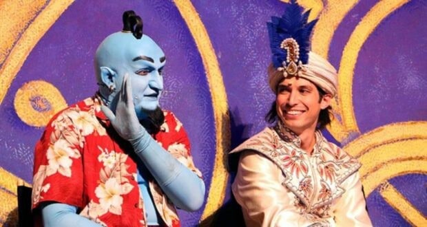 Genie and Aladdin, brought to life by performers in vibrant costumes, grin for the camera against a magical purple backdrop—capturing the joy of meeting beloved Disney characters in the park, while fans fondly remember performer Billy Kametz and his legacy.