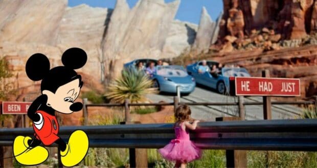 Mickey Mouse, looking uncharacteristically downcast, sits beside a young guest dressed in pink near the Radiator Springs Racers attraction, with Cars Land’s signature rocky backdrop completing the scene.