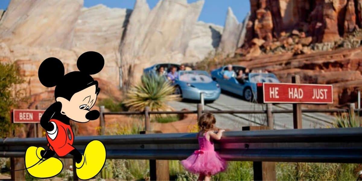 Mickey Mouse, looking uncharacteristically downcast, sits beside a young guest dressed in pink near the Radiator Springs Racers attraction, with Cars Land’s signature rocky backdrop completing the scene.