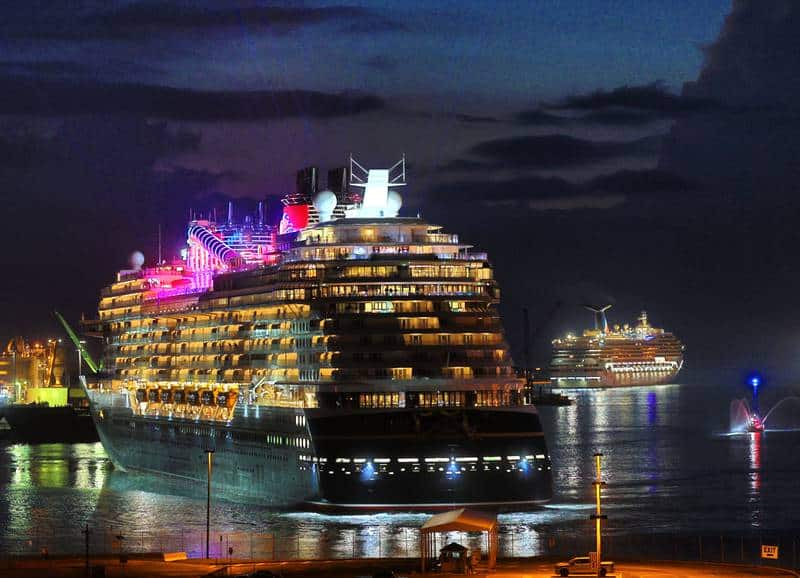 The Disney Wish, illuminated with dazzling lights, arrives at Port Canaveral alongside other cruise ships at night, casting vibrant reflections across the harbor waters—a magical scene for Disney fans and cruisers alike.