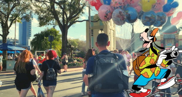 Disney World buzzes with energy as families stroll past cheerful balloons, while Goofy snaps photos in the foreground—showcasing must-have Disney backpack essentials for a magical day of fun and adventure.