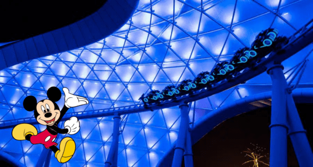 Mickey Mouse greets fans near the thrilling TRON Lightcycle / Run roller coaster at Disney World, surrounded by vibrant blue lighting and dazzling displays as excited riders race by under the night sky.