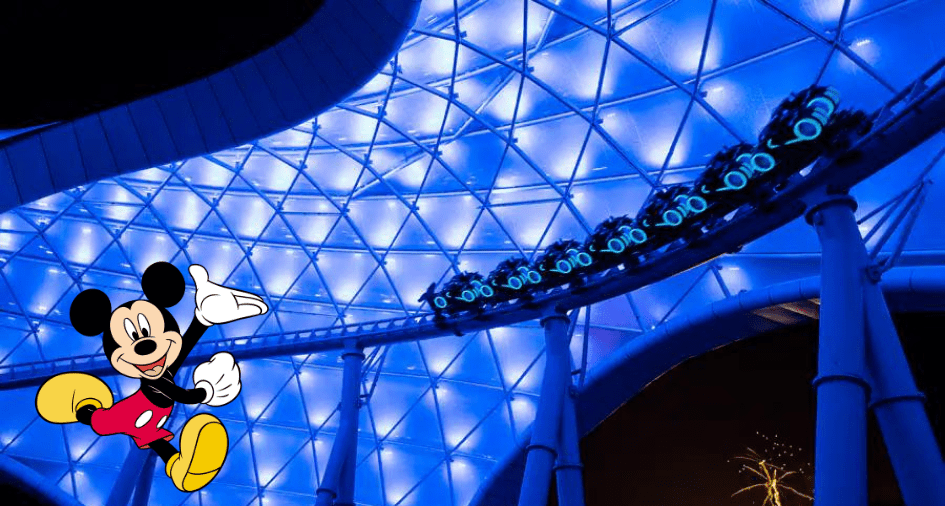 Mickey Mouse greets fans near the thrilling TRON Lightcycle / Run roller coaster at Disney World, surrounded by vibrant blue lighting and dazzling displays as excited riders race by under the night sky.