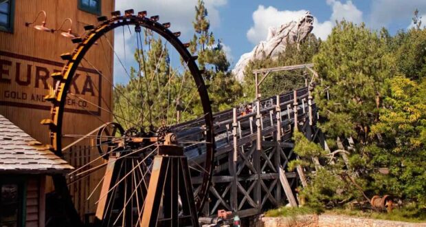 The iconic water wheel spins next to the wooden tracks of Grizzly River Run at Disney California Adventure, framed by lush trees and rugged mountain scenery—capturing the thrilling atmosphere of this beloved attraction, recently in the spotlight after a guest’s unexpected jump prompted an evacuation.