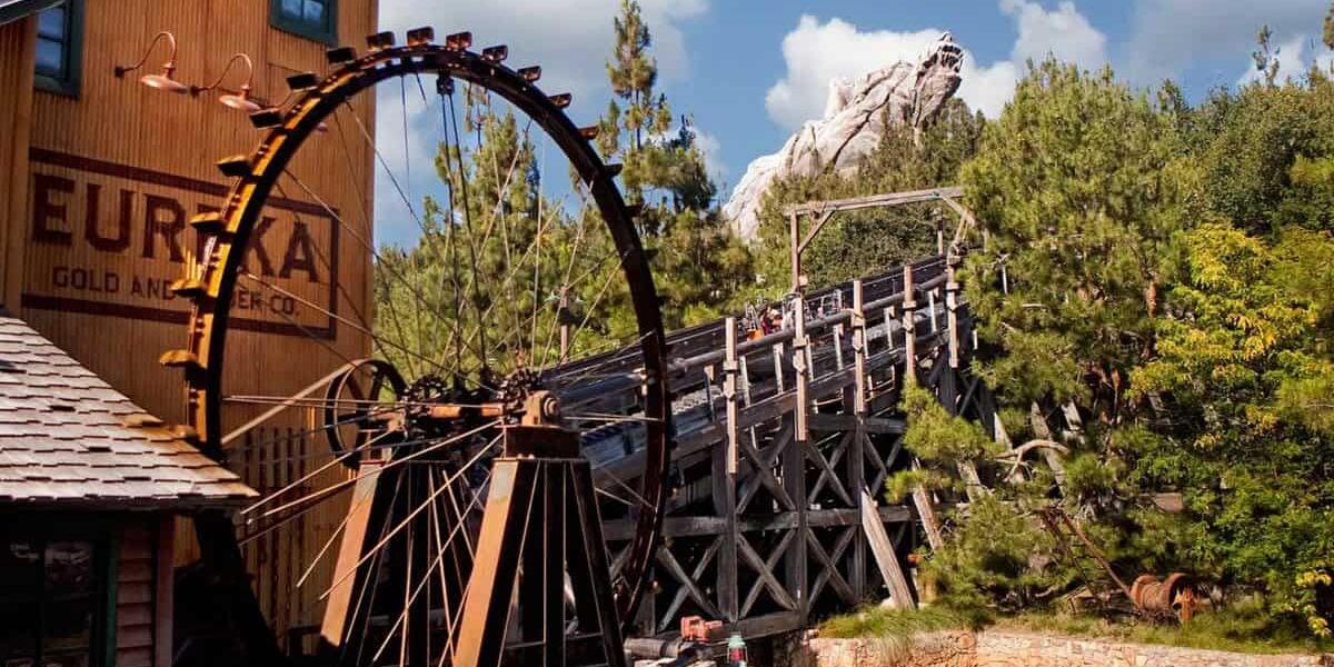 The iconic water wheel spins next to the wooden tracks of Grizzly River Run at Disney California Adventure, framed by lush trees and rugged mountain scenery—capturing the thrilling atmosphere of this beloved attraction, recently in the spotlight after a guest’s unexpected jump prompted an evacuation.