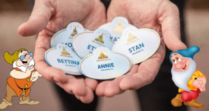 Disney Cast Member name tags are held up, flanked by two smiling cartoon dwarfs from Snow White admiring the tags—capturing that heartwarming Disney magic perfect for sharing a Cast Compliment.