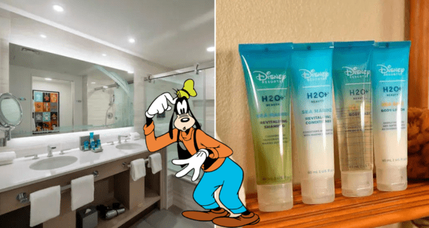 Goofy poses by the bathroom counter inside a Disney H2O Resort room, with a lineup of Disney H2O+ bath products ready for guests.