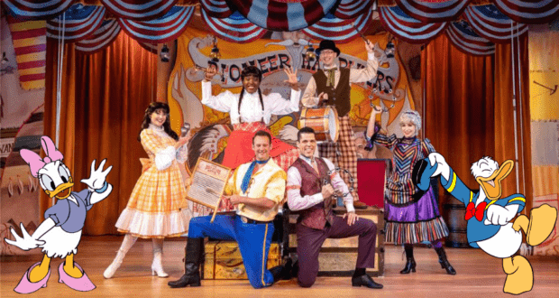On stage at Disney's Hoop-Dee-Doo Musical Revue, six lively performers join Daisy and Donald Duck in front of a charming Pioneer-themed backdrop, capturing the beloved show's spirited energy.