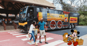 Excited families make their way past a whimsical Sunshine Flyer train-themed bus, while Mickey Mouse, ready for adventure with his luggage, welcomes guests in the corner.
