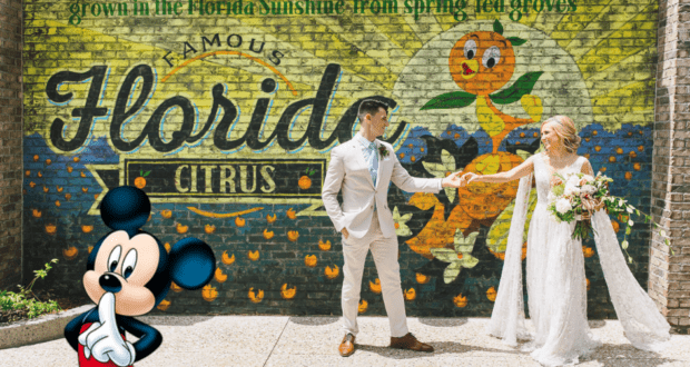 Mickey Mouse greets a happy bride and groom posing by a vibrant Florida Citrus mural at Disney World, capturing the magic of dream weddings made affordable with Budget Disney Weddings.
