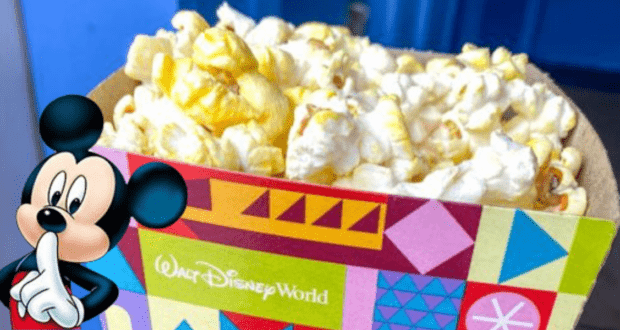 A vibrant Disney Popcorn box at Magic Kingdom, starring Mickey Mouse on the front, playfully holding a finger to his lips with a "shh" as part of the magical theme park experience.