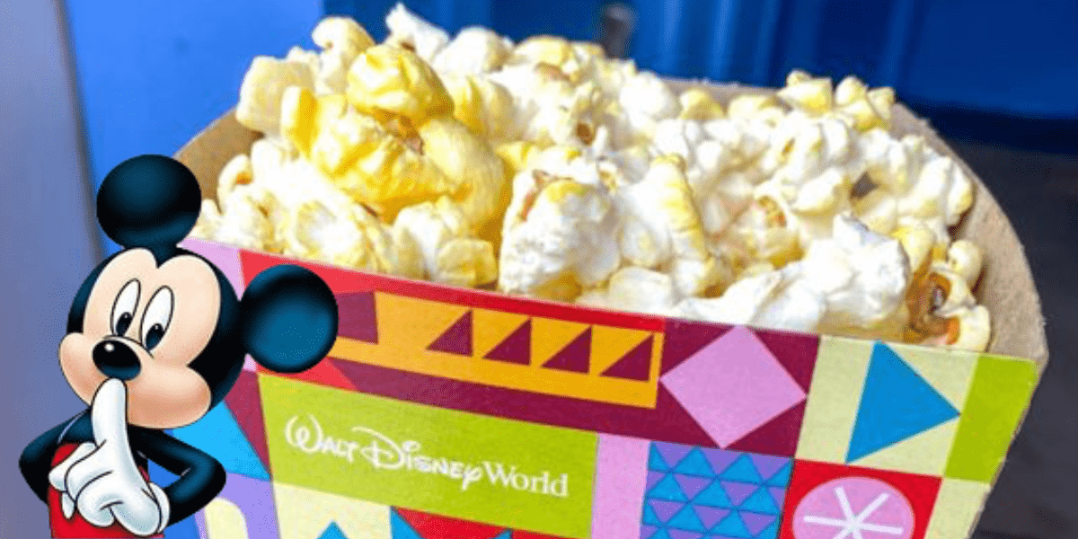 A vibrant Disney Popcorn box at Magic Kingdom, starring Mickey Mouse on the front, playfully holding a finger to his lips with a "shh" as part of the magical theme park experience.