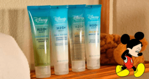 A set of four Disney H2O+ toiletries is perfectly lined up next to a sponge, topped off with Mickey Mouse appearing in the bottom right corner to add that signature Disney magic to your resort bathroom essentials.