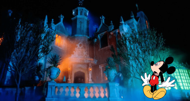 The iconic Haunted Mansion glows an eerie blue at night, with the infamous Hatbox Ghost casting a chilling presence in the shadows while Mickey Mouse reacts in surprise at the scene nearby.