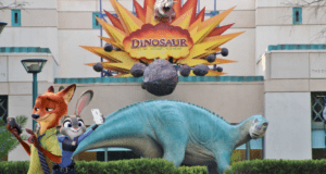 Nick and Judy from Zootopia snap selfies together in front of the giant dinosaur statue at Dinoland, capturing their adventure at this fun-filled family attraction.
