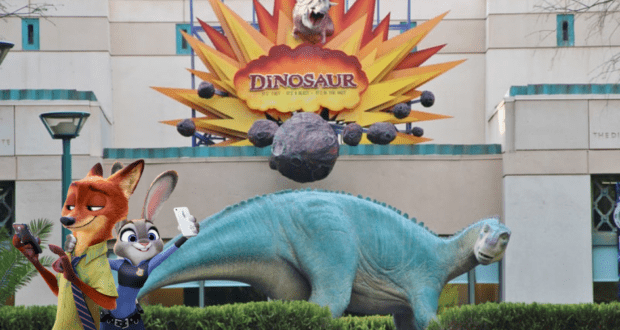 Nick and Judy from Zootopia snap selfies together in front of the giant dinosaur statue at Dinoland, capturing their adventure at this fun-filled family attraction.