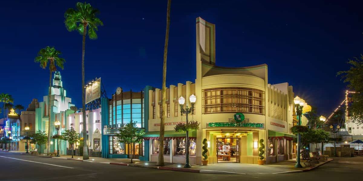 Art Deco-style buildings brightly illuminated against the night sky, with palm trees framing an empty avenue—evoking the iconic ambiance of Hollywood Boulevard at Disney’s Hollywood Studios after hours, where the lights create a dramatic, movie-set stillness reminiscent of moments just after a show or parade has ended.