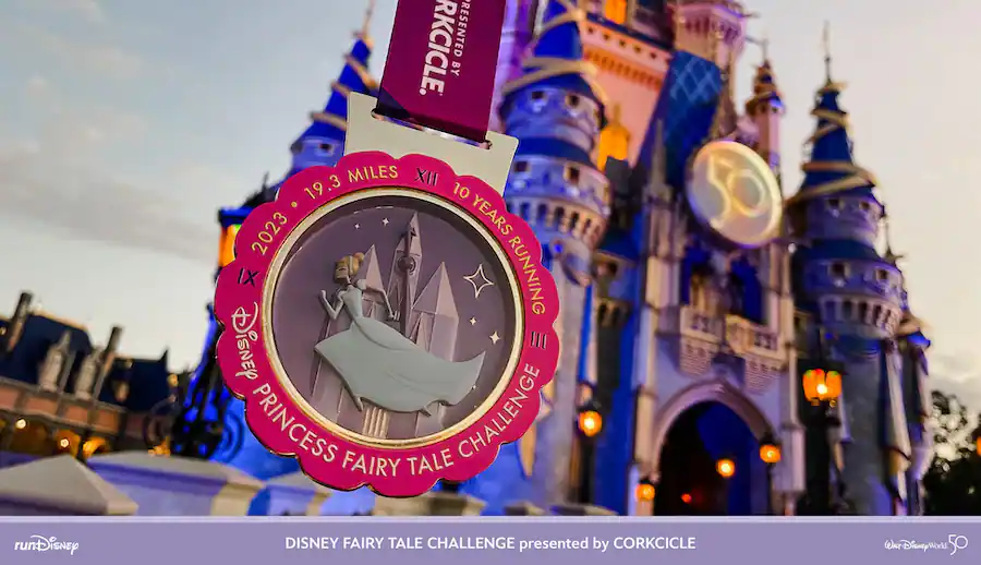Cinderella shines on the Disney Princess Fairy Tale Challenge medal, held proudly in front of Cinderella Castle at sunset, celebrating the accomplishment of finishing the Disney Princess Half Marathon at Walt Disney World.
