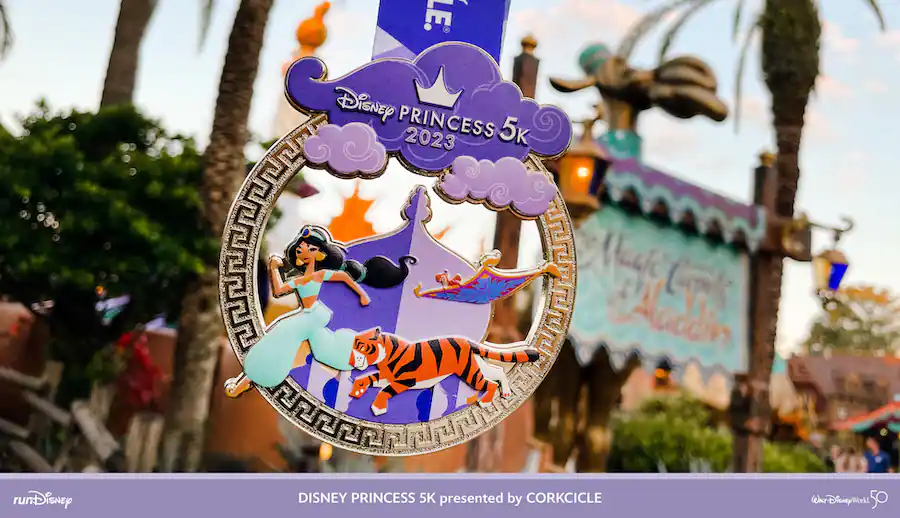 The Disney Princess 5K 2023 medal showcases Jasmine, Rajah, and the magic carpet in vibrant detail, displayed outside as part of the festivities for Disney Princess Half Marathon Weekend at Walt Disney World.