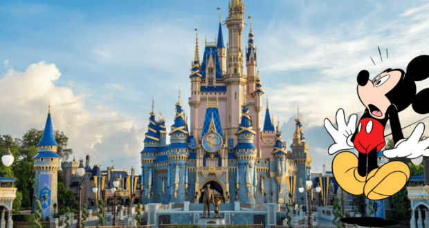 Mickey Mouse looks surprised in front of the iconic blue and gold fairytale castle at Disney World, with clouds overhead and an armful of charming Disney merchandise from Magic Kingdom’s Big Top Souvenirs peeking out.