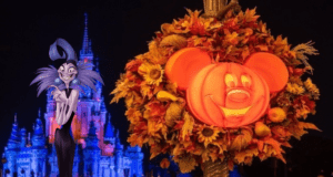 Mickey-shaped pumpkin wreath adorned with autumn leaves welcomes guests as Cinderella Castle glows blue in the background. A Disney Villain, dressed in vibrant purple, strikes a pose to the left—capturing the enchanting atmosphere of a Disney Halloween Party.
