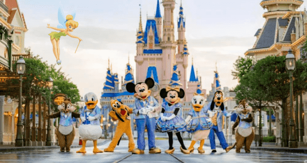 Mickey Mouse, Minnie, Goofy, and other beloved Disney characters gather in front of Cinderella Castle as Tinker Bell soars overhead under clear blue skies. The magic stretches into the night with dazzling experiences during Disney World’s Extended Evening Hours.