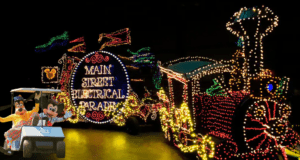The Main Street Electrical Parade train glimmers in the night at Walt Disney World, its signature sign illuminating the enchantment of the park. Nearby, Goofy and Max beam from their golf cart, looking ready to join in the dazzling nighttime celebration.