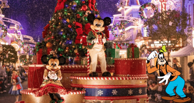 Mickey and Minnie, dressed in their holiday best, pose by a sparkling Christmas tree during Mickey's Very Merry Christmas Party at Magic Kingdom, with Goofy nearby waving to guests.