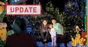 Three happy kids take a festive photo in front of sparkling Christmas trees at the Night of a Million Lights, joined by Pluto for a magical holiday moment.