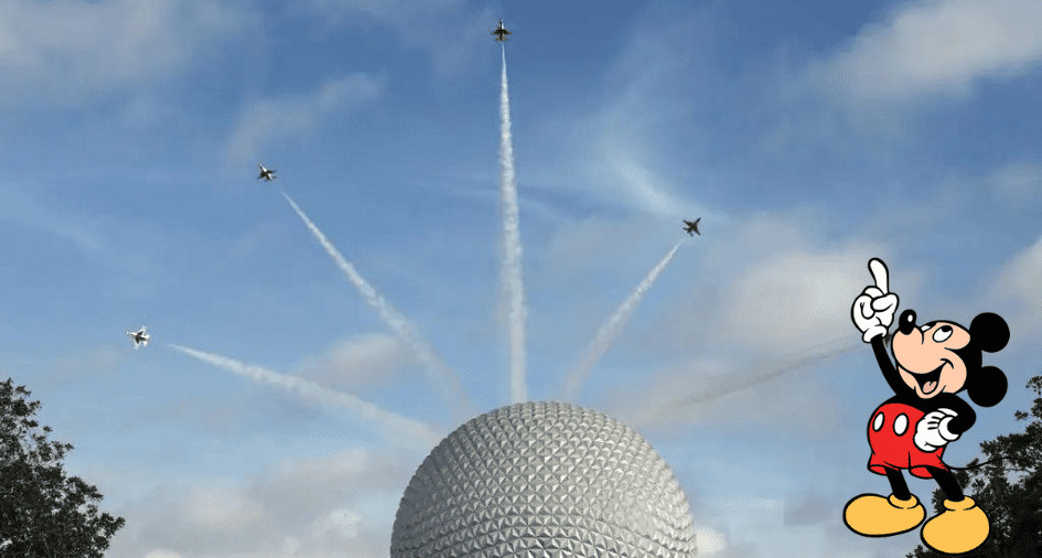Mickey Mouse excitedly points toward an awe-inspiring Thunderbird Flyover above Epcot’s iconic geodesic sphere, as jets streak across the brilliant blue sky trailing dazzling white smoke during a magical day at Disney World.