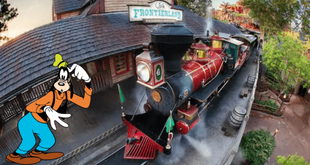 Goofy greets guests beside a classic red train at the Walt Disney World Railroad’s Frontierland Station, with lush trees creating a magical backdrop in the heart of the park.