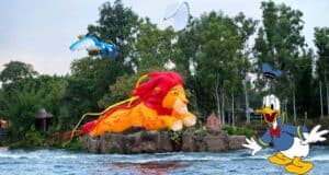 Lion and bird-shaped kites soar above the water in a colorful Disney KiteTails performance at Walt Disney World, while Donald Duck grins near the edge of Discovery River.