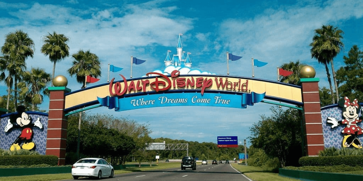 Walt Disney World entrance with Mickey and Minnie, vibrant flags, “Where Dreams Come True,” energizing buzz about a fifth gate.