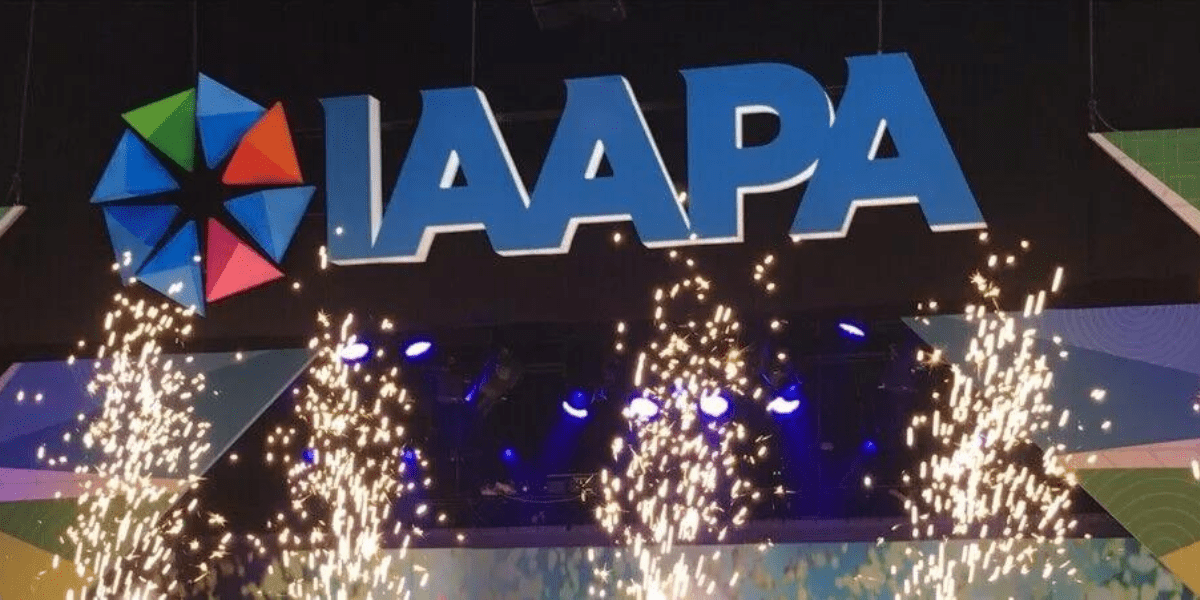 The IAAPA Expo 2022 sign with its vibrant logo shines above a display of stage lights, as dazzling bursts of fireworks capture the excitement and spectacle celebrated by the attractions industry.