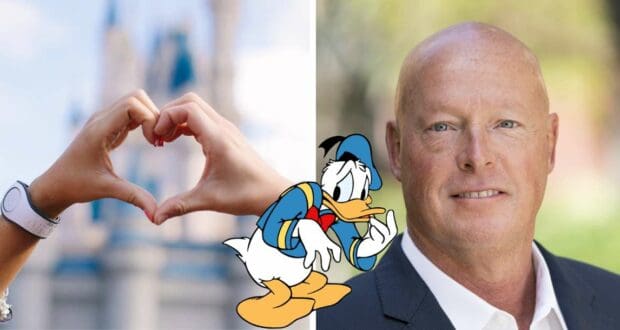 Guests create a heart shape with their hands around Donald Duck center stage, while a sharply dressed Disney executive beams nearby—perhaps reflecting on recent company changes amid the magic.