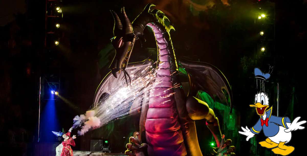 Maleficent the dragon breathes fire across the Fantasmic! stage under the night sky, while Donald Duck appears in animated form at the lower right, capturing an unforgettable Disney World spectacle.