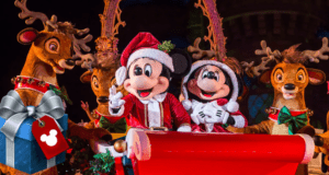 Mickey and Minnie Mouse don festive Santa outfits as they lead a vibrant Disney Christmas parade, joined by reindeer and a sparkling blue gift box. The scene is brimming with holiday spirit, all in support of the Ultimate Toy Drive at Disney Parks.