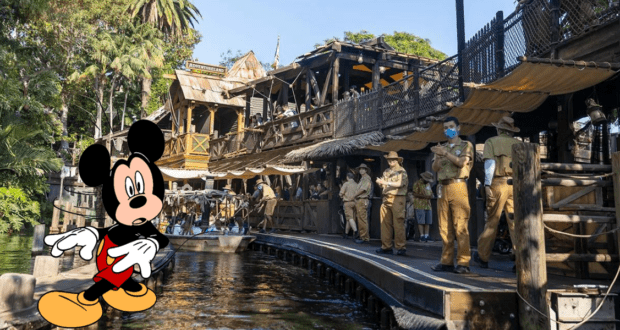 Mickey Mouse greets guests along the riverside dock of the Jungle Cruise at Disney World, surrounded by cast members in classic explorer uniforms and rustic Adventureland architecture. The scene feels lively and immersive, but there’s an undercurrent of mystery—almost as if Adventureland hides a secret just beyond its cheerful facade.