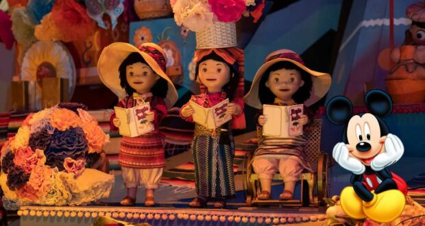 Three vibrant dolls dressed in colorful attire sing joyfully with books in hand, surrounded by whimsical flowers, while Mickey Mouse sits nearby amidst the playful scenery, capturing the enchanting spirit of Disney’s "it’s a small world" attraction.