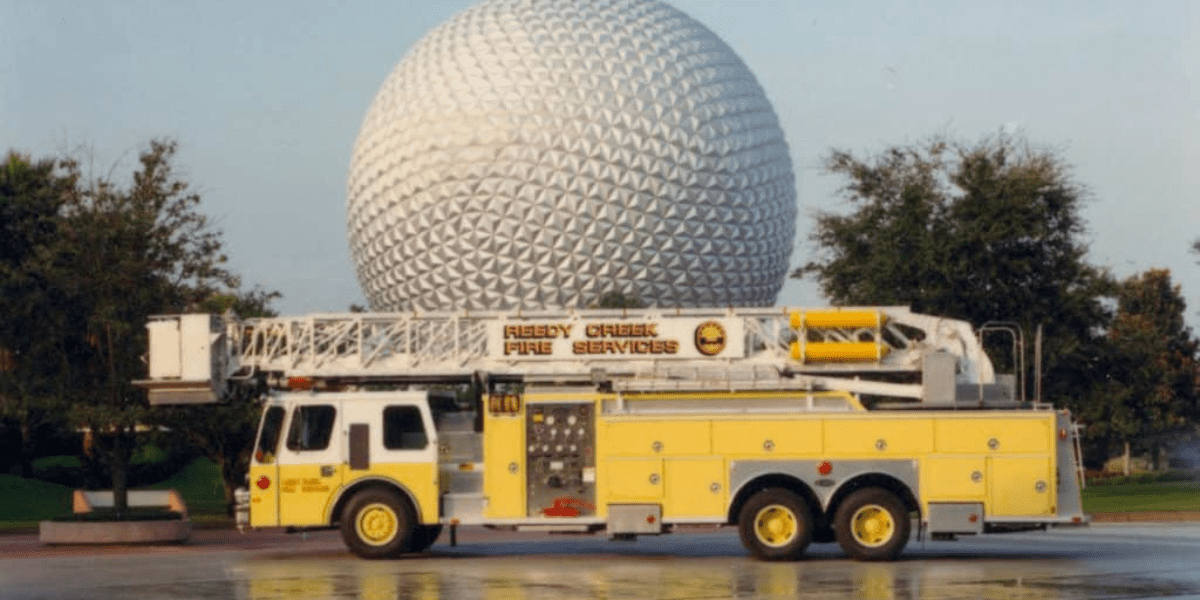 A bright yellow Reedy Creek fire truck bearing the "Reedy Creek Fire Services" logo is parked right in front of Epcot’s iconic Spaceship Earth geodesic sphere at Walt Disney World.