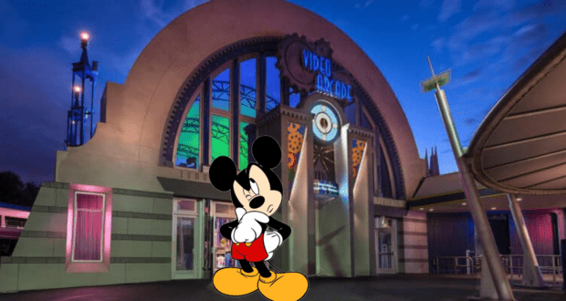 Mickey Mouse pauses thoughtfully at dusk in front of the vibrant, retro-themed Tomorrowland Light & Power Co. arcade at Disney World.