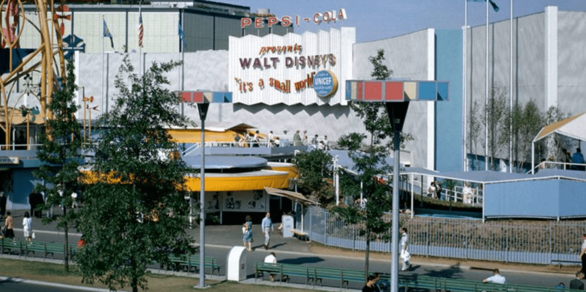 The iconic "It's a Small World" entrance at Disney, featuring classic Pepsi-Cola signage and World’s Fair-inspired architecture, welcomes guests as visitors stroll by.