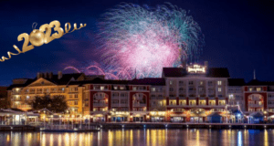 Dazzling fireworks light up the night sky above Disney’s BoardWalk Inn, reflecting on Crescent Lake as a shimmering gold “2023” graphic glows in the corner—celebrating New Year’s Eve at Walt Disney World with signature magic and excitement.