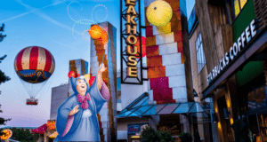 The Fairy Godmother waves her wand in front of vibrant Disney Village storefronts and the iconic Starbucks, all aglow with the magic of sunset near Disneyland Paris.