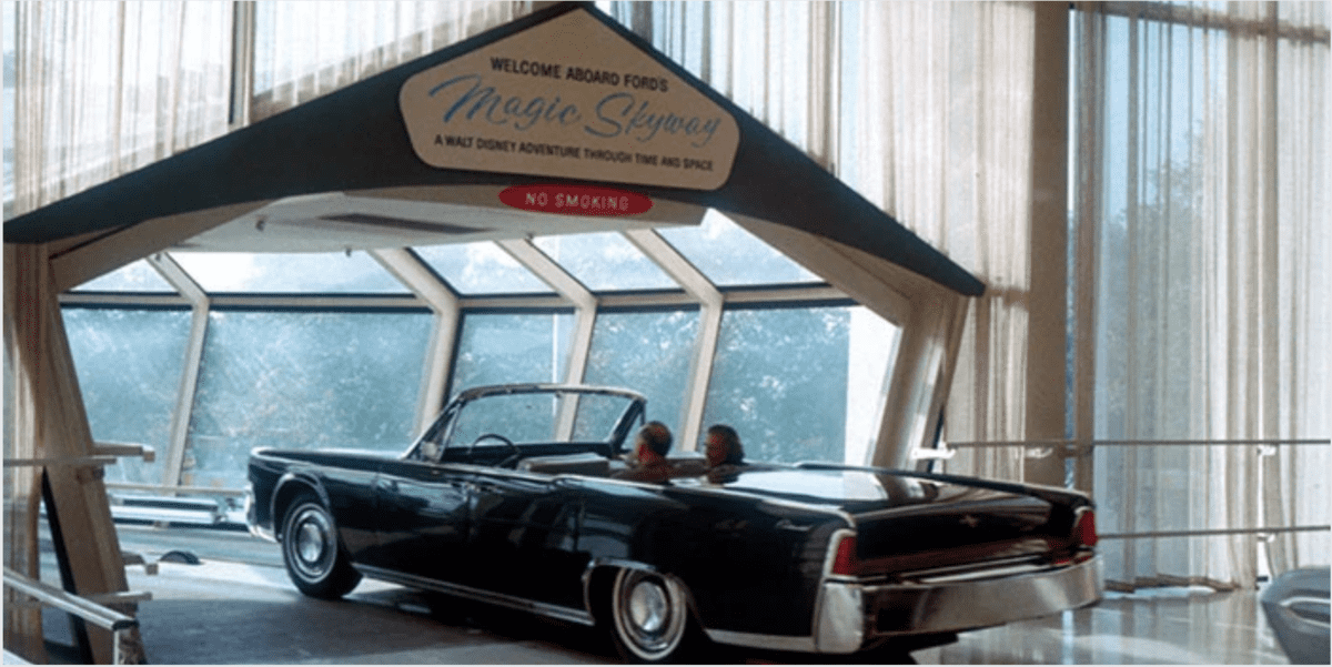 A sleek black convertible cruises beneath the iconic "Magic Skyway" sign inside a pavilion, capturing the nostalgic spirit of Disney World's Fair attractions with two guests enjoying the ride.