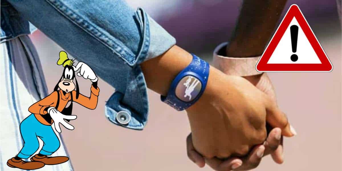 Guests clasp hands near a playful Goofy cartoon and a bold red warning sign with an exclamation mark—one guest shows off their MagicBand implant.